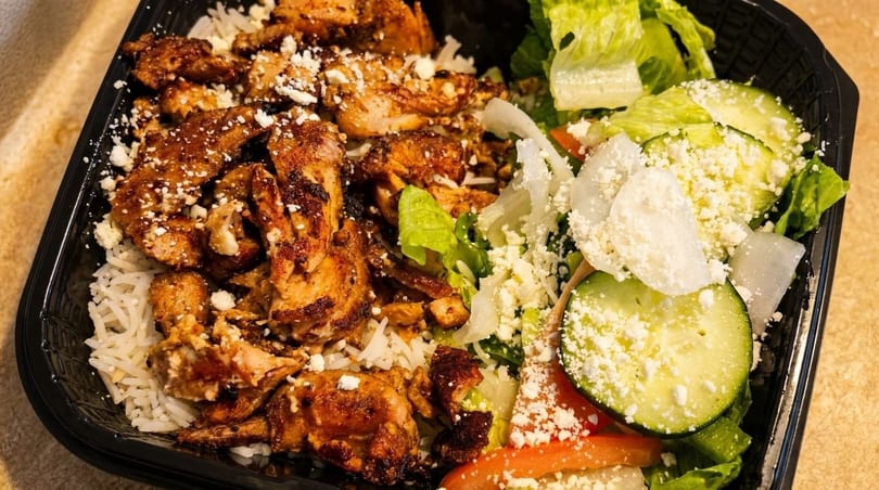 Grilled chicken and rice with a side salad topped with feta cheese in a black container.